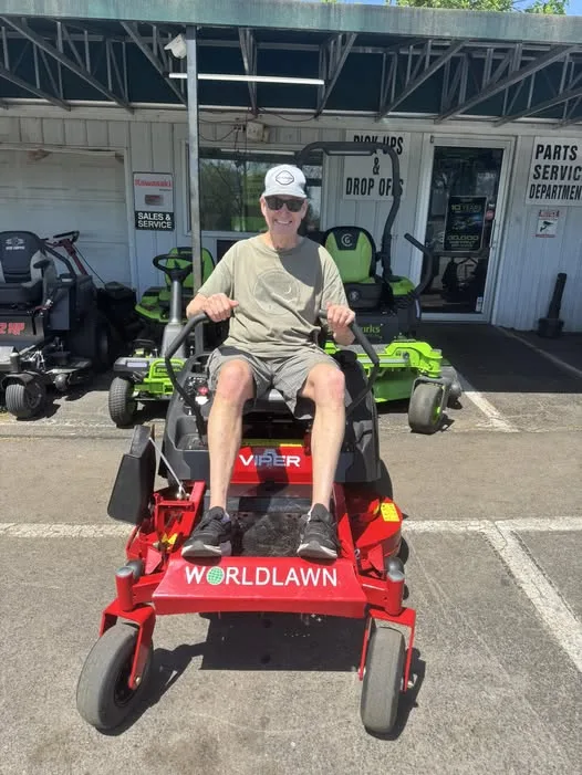 Customer seated on a red Worldlawn Viper zero-turn mower outside the shop