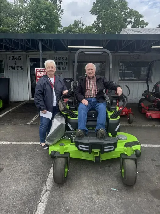 Two customers with a green zero-turn mower outside Mobile Mower Repair