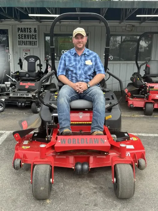 Customer seated on a red Worldlawn zero-turn mower outside the shop
