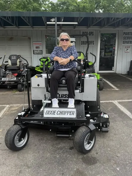 Customer seated on a silver Dixie Chopper zero-turn mower outside the shop
